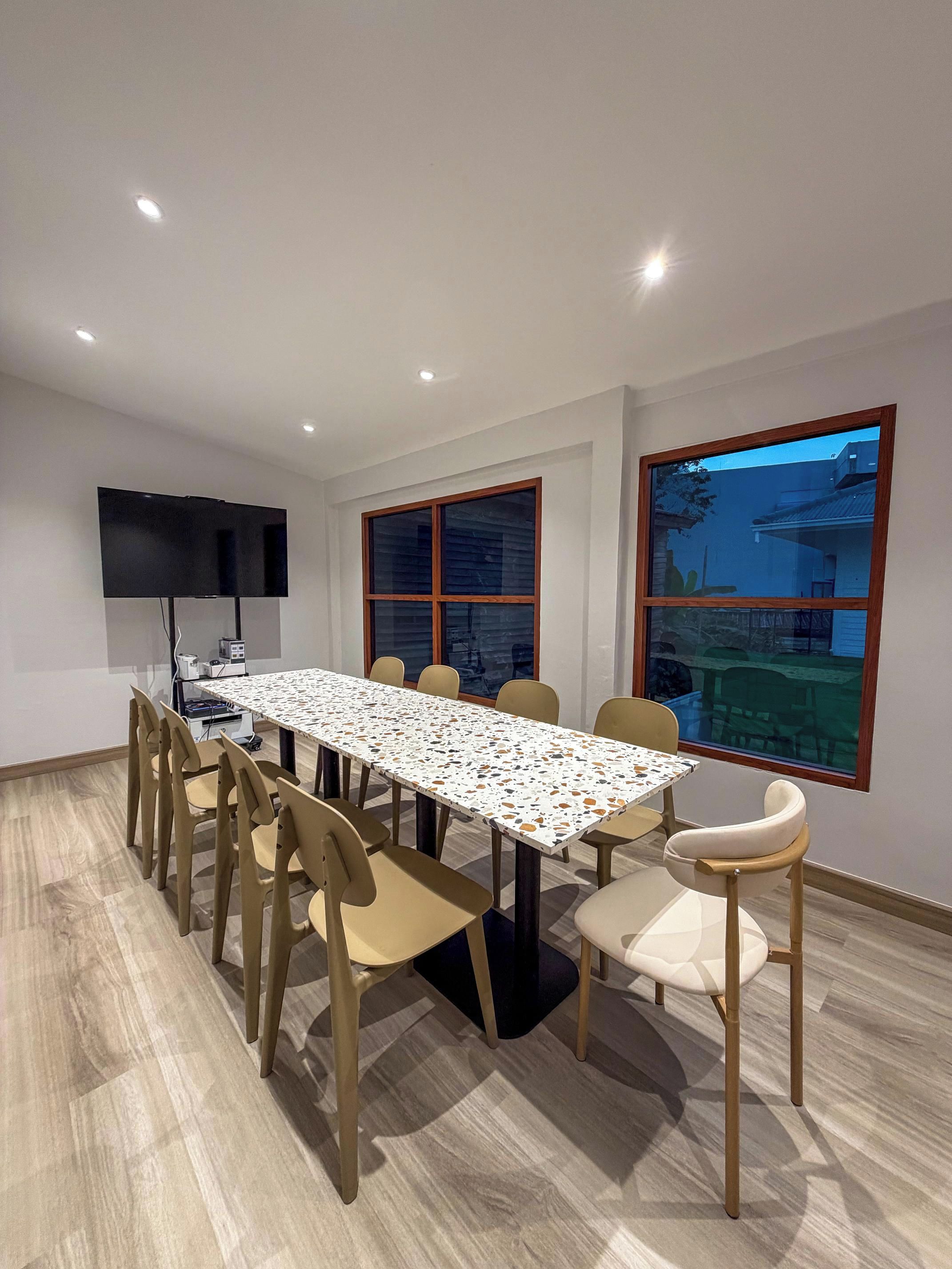 A conference room with a long table, chairs, a flat-screen TV, and windows.