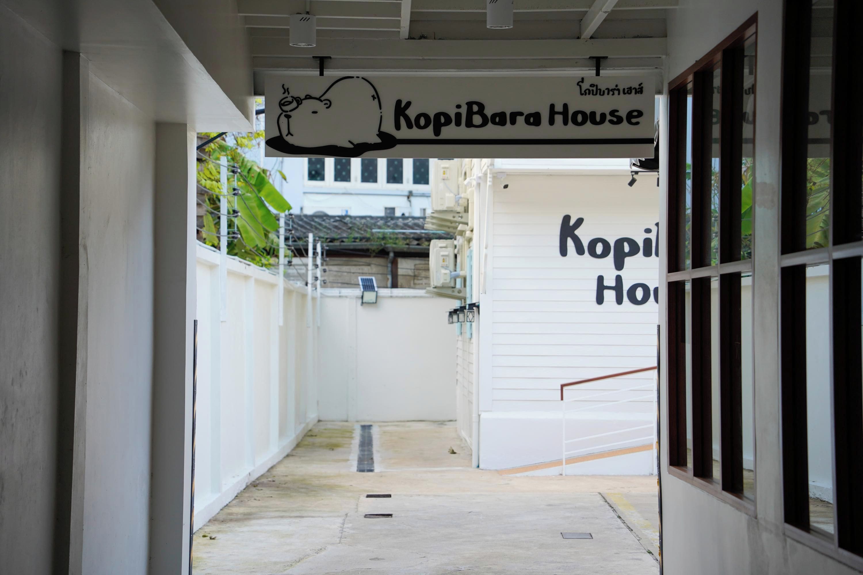 A corridor leading to a building with a sign reading 'KopiBara House'.