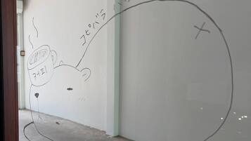 A room with white walls, a concrete floor, and a large window. There is a drawing of a bear and a cup on the wall.