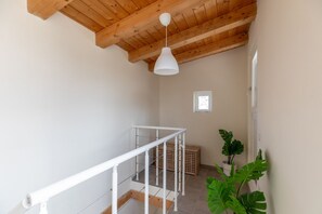 Un escalier avec un plafond en bois et une rampe blanche, menant à un palier doté d’une petite fenêtre.