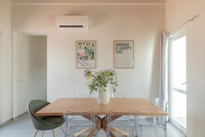 Ein moderner Essbereich mit einem Holztisch, transparenten Stühlen und einer Vase mit Blumen. An der Wand hängen zwei gerahmte Bilder.