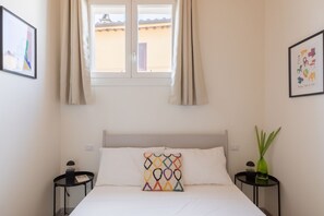A hotel room with a bed, two bedside tables, a window with curtains, and a wall with framed artwork. - iFlat | Scenic Penthouse with Terrace near Vatican (Rome)