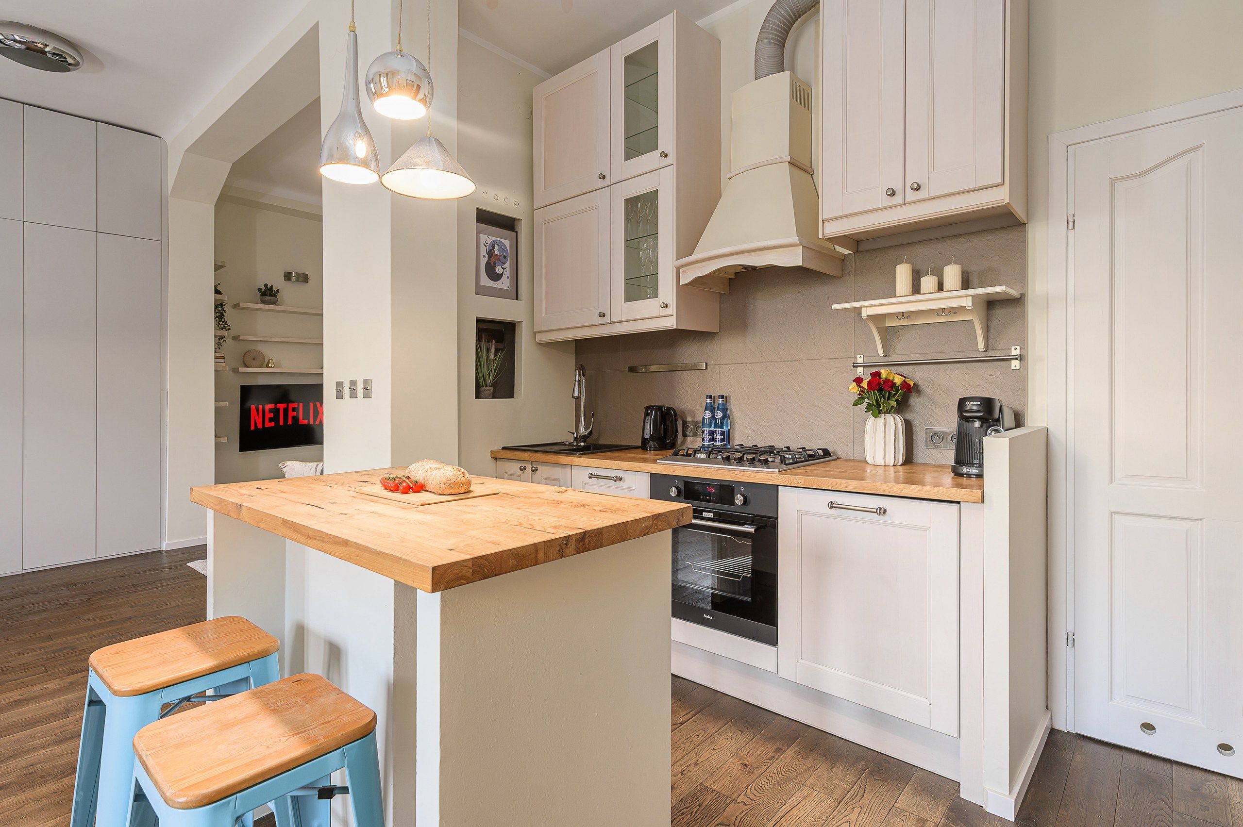 A modern kitchen with white cabinetry, a wooden island, and blue bar stools.