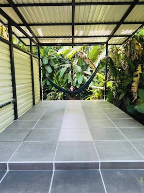 Ein überdachter Patio-Bereich mit einer Hängematte, Fliesenboden und üppiger tropischer Bepflanzung.