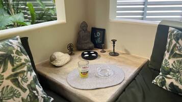 Un coin douillet avec un banc rembourré, une petite table avec un set de table, une statue de Bouddha, un panneau encadré, un chandelier et un coquillage décoratif.