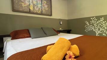 A hotel room with a bed, pillows, a painting, an air conditioner, and a wall decoration.