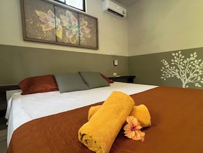 Ein Hotelzimmer mit einem Bett, Kissen, einem Gemälde, einer Klimaanlage und Wanddekoration.