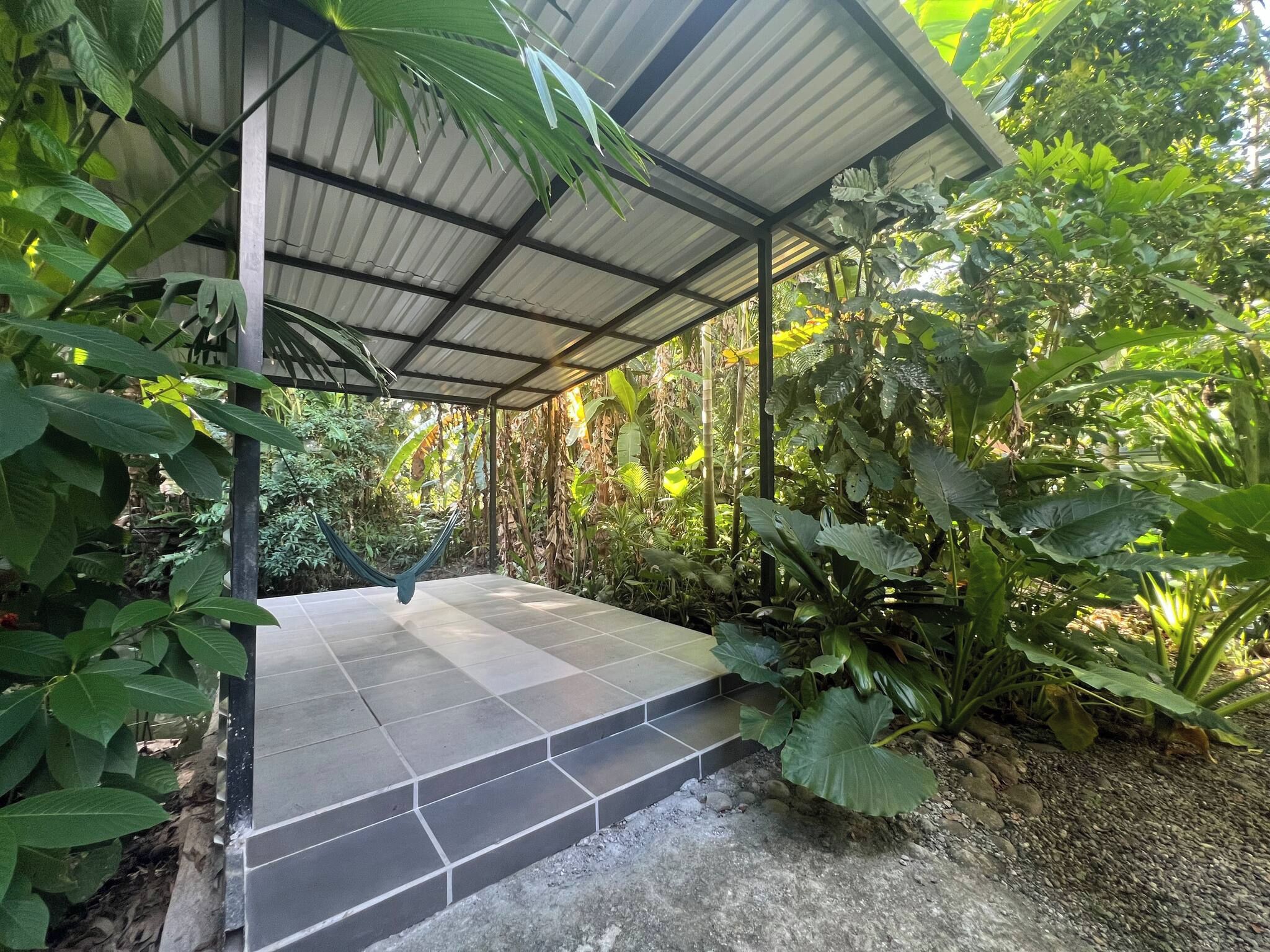 Un espace extérieur abrité, doté d’un sol carrelé et entouré d’une végétation luxuriante.