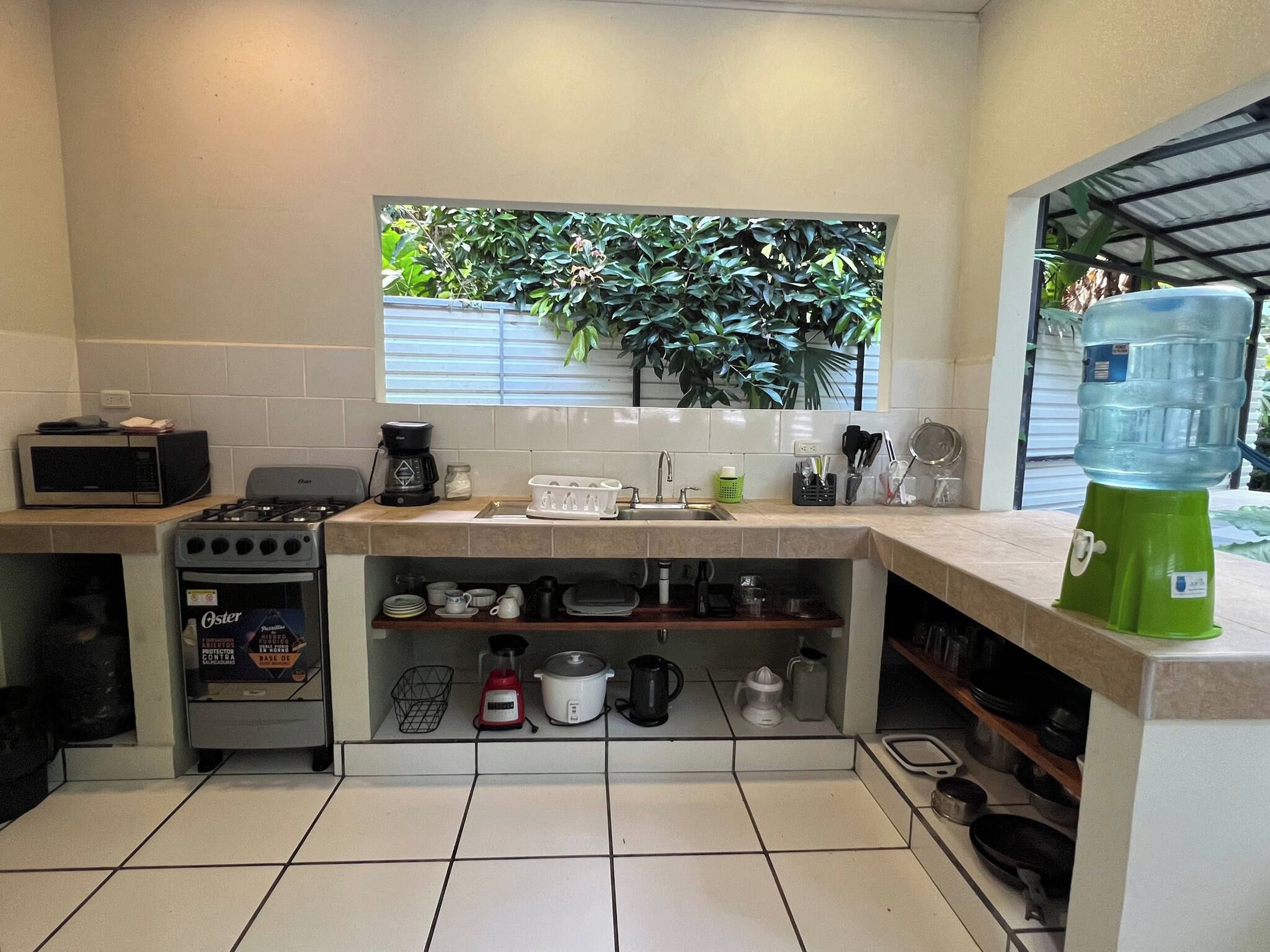 Cocina compacta con microondas, estufa y pileta. Se ve un ventanal con vista a la vegetación.