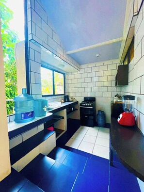 Une cuisine compacte équipée d’une cuisinière à gaz, d’un distributeur d’eau et d’un mixeur posés sur le plan de travail.