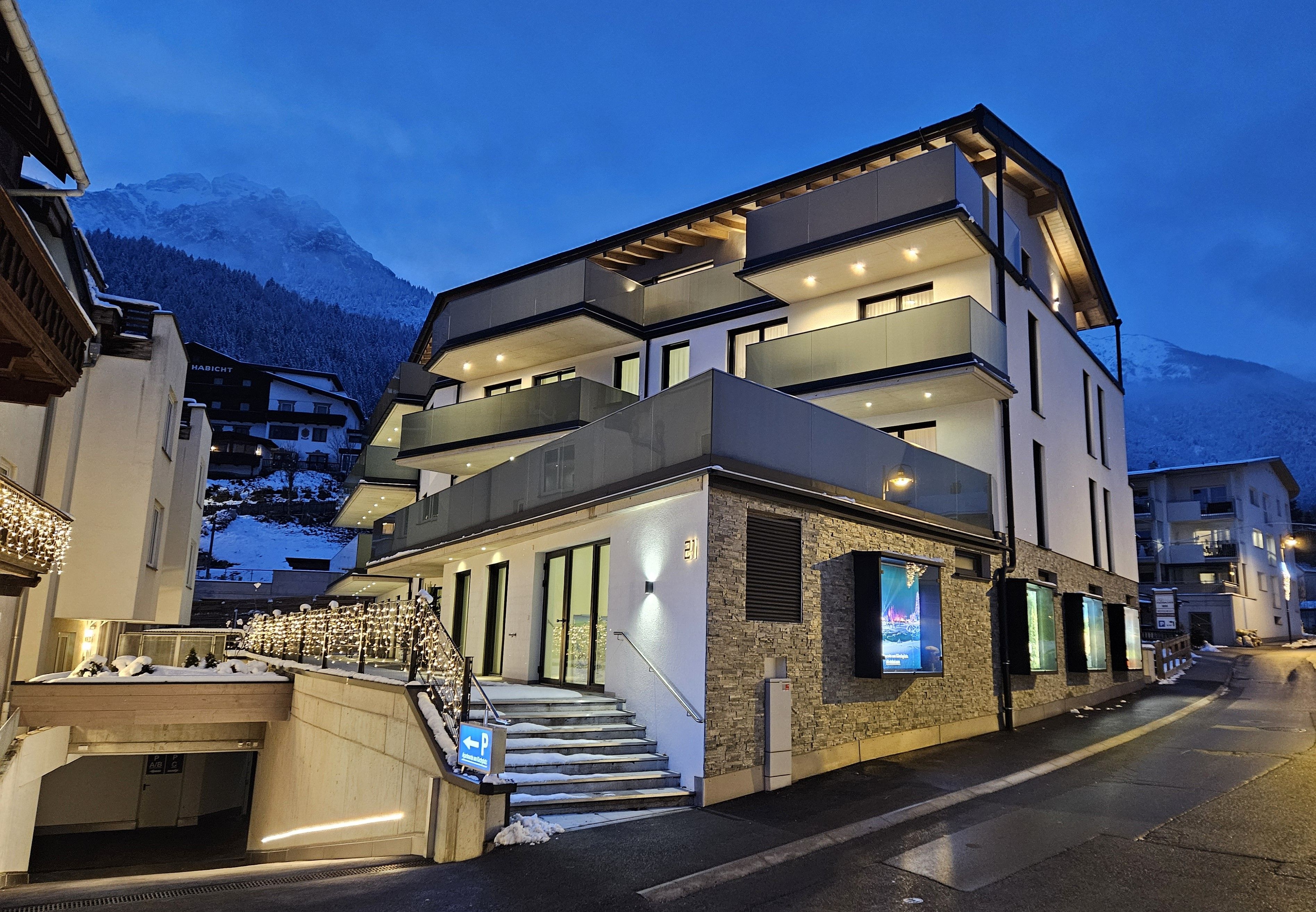 A multi-story hotel with a modern design, featuring balconies, large windows, and a staircase leading to the entrance.