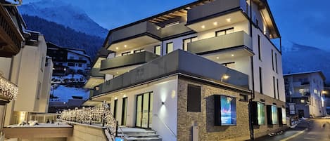 A multi-story hotel with a modern design, featuring balconies, large windows, and a staircase leading to the entrance.