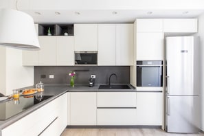 A modern kitchen with white cabinets, a black countertop, a stainless steel refrigerator, and a built-in oven. - iFlat | Sleek & Sunlit Apartment near the Vatican (Rome)