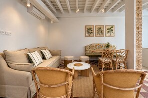 A living room with a sofa, two armchairs, a small table, and a dining area with a table and chairs. There are wall-mounted air conditioning units and a window with a view. - Genteel Home Patio del Arenal Terrace 301 (Seville)