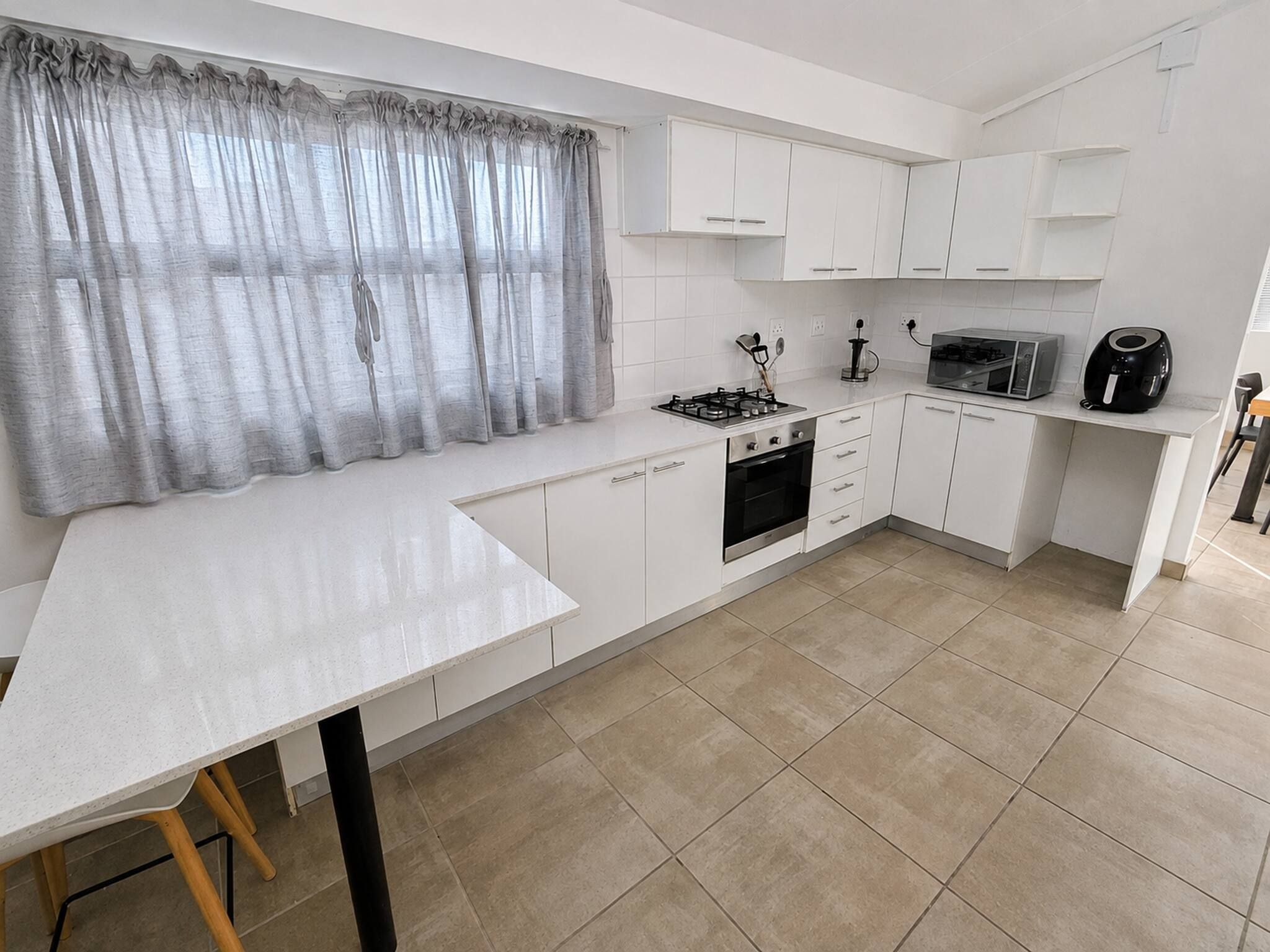 A modern kitchen with white cabinetry, a gas stove, an oven, a microwave, and a coffee maker.