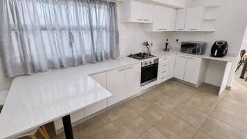 A modern kitchen with white cabinetry, a gas stove, an oven, a microwave, and a coffee maker.