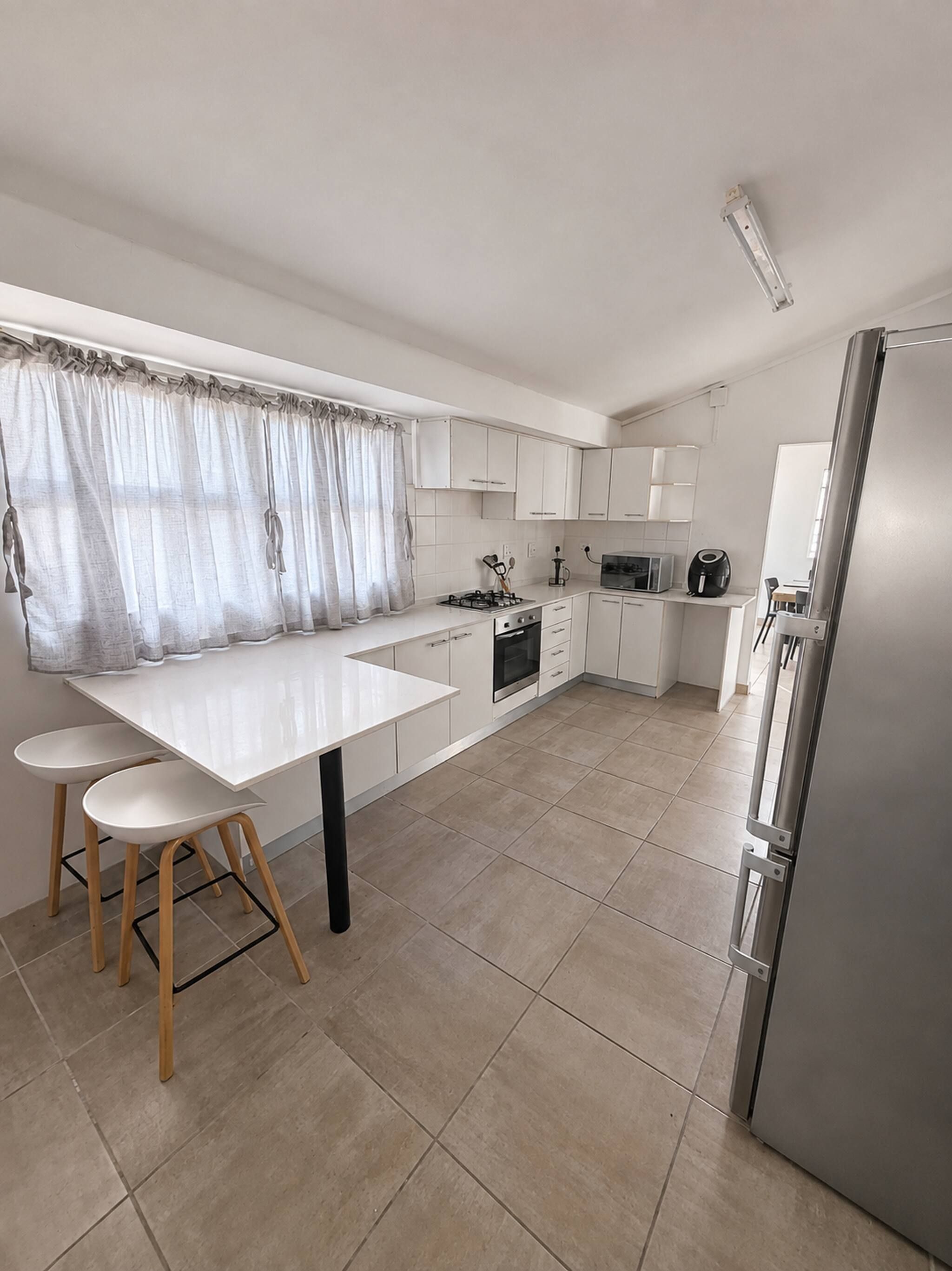 Une cuisine moderne avec des meubles blancs, un îlot central doté de tabourets, un four encastré et un réfrigérateur.