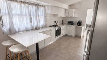Une cuisine moderne avec des meubles blancs, un îlot central doté de tabourets, un four encastré et un réfrigérateur.