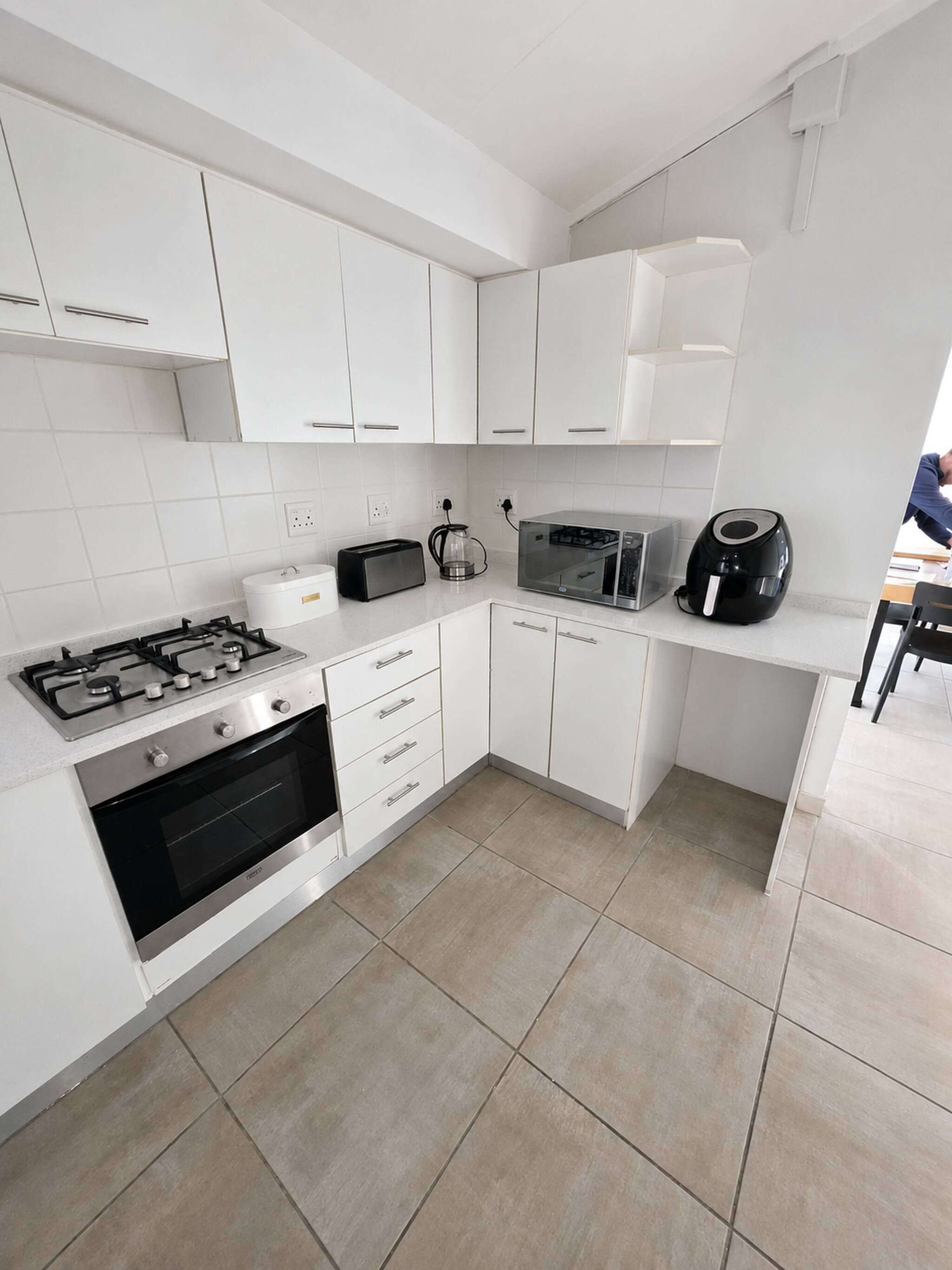 A modern kitchen with white cabinetry, a gas stove, an oven, a microwave, and a coffee maker.