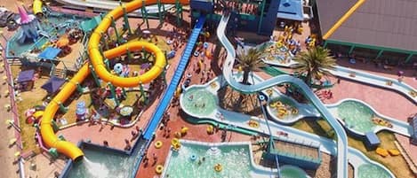 A water park with multiple slides and pools, surrounded by a parking area and buildings.