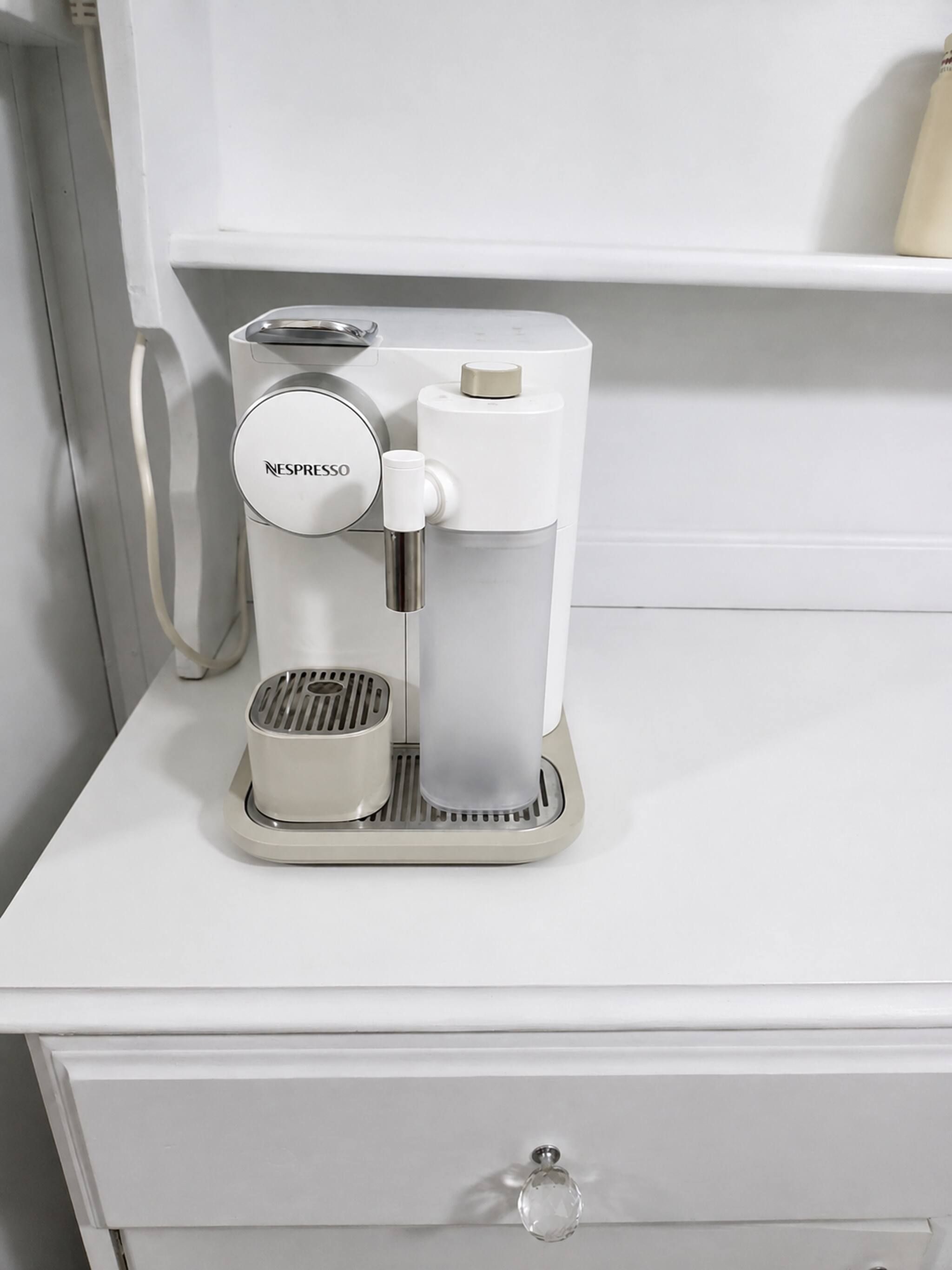 A Nespresso coffee machine on a white countertop with a drawer below.