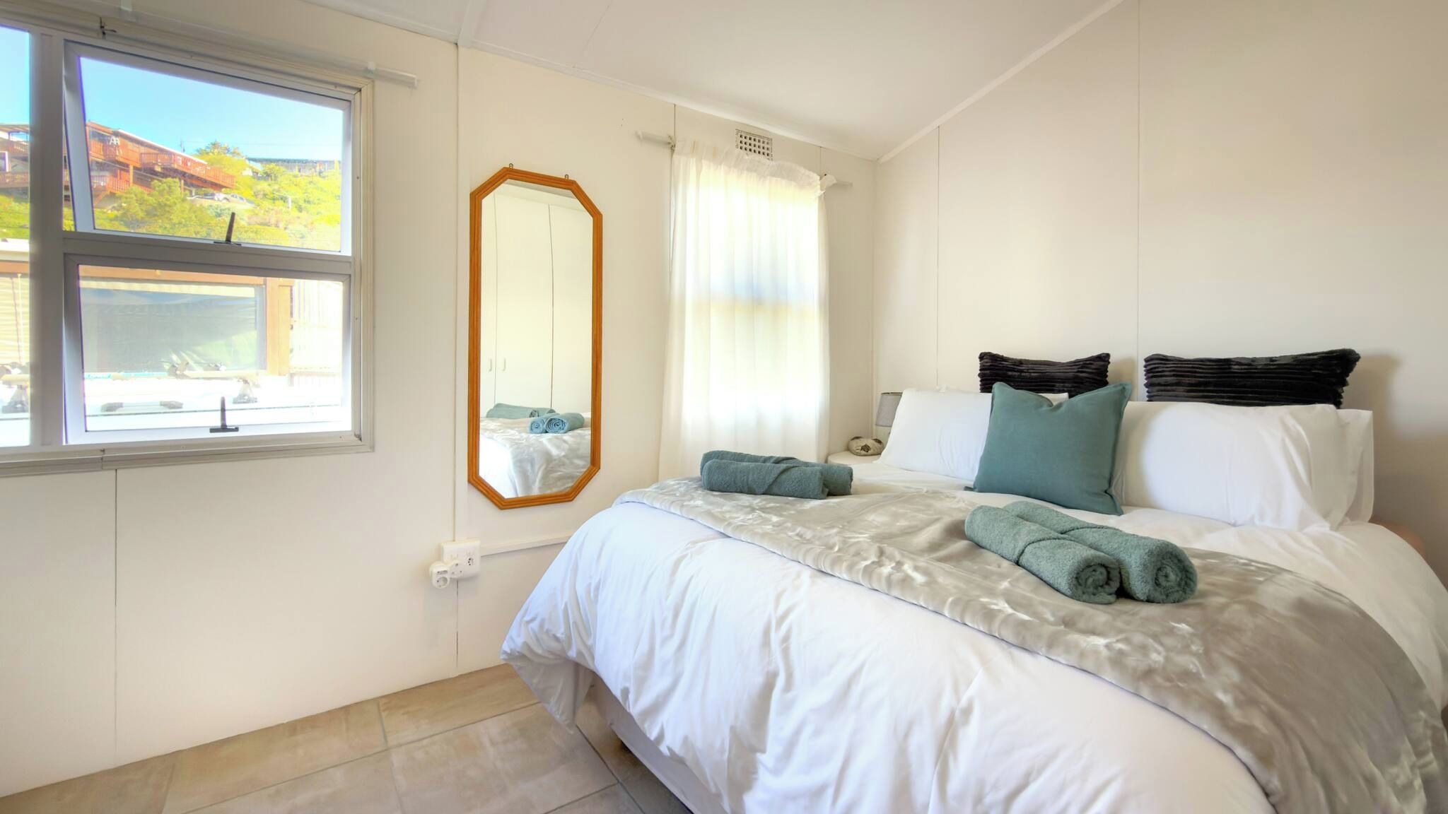 A bedroom with a bed, a large mirror, a window, and a view of a train.