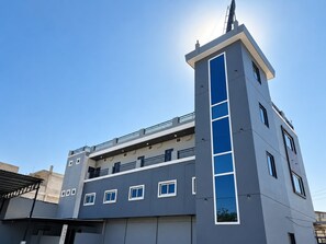 Un edificio de varios pisos con una llamativa banda vertical azul, balcones y cielo despejado.