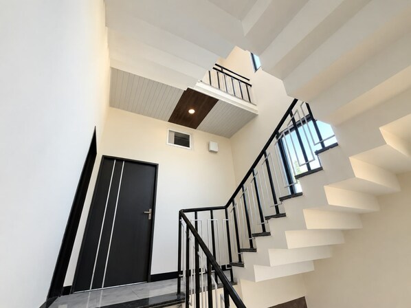 A modern staircase with a black railing and white walls, leading to a landing with a small window.