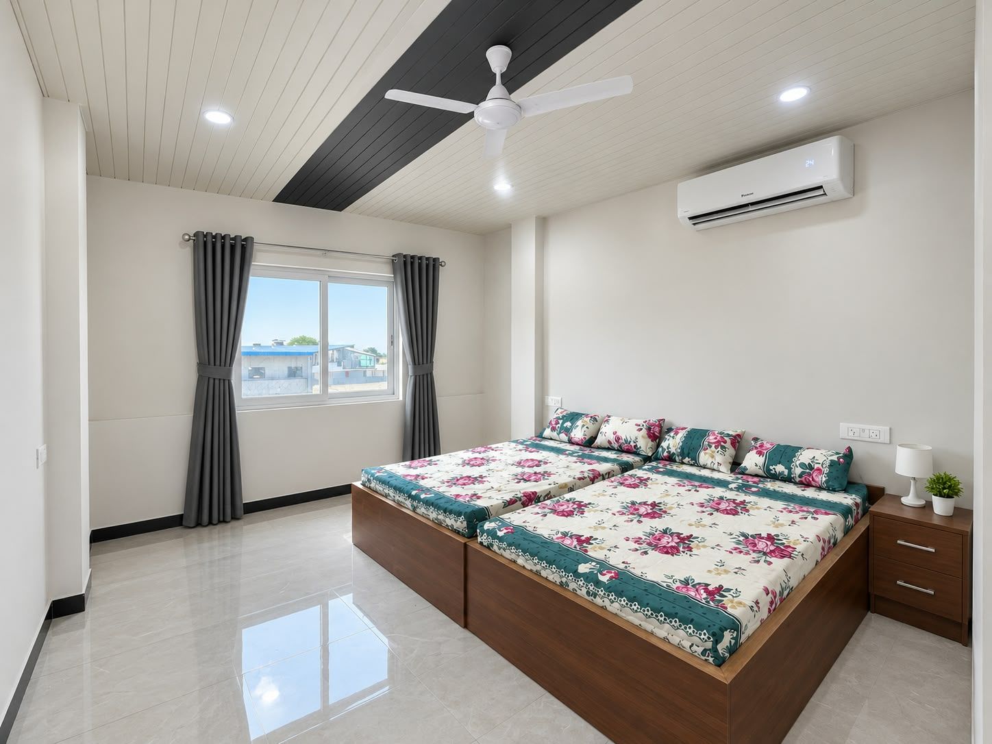 A bedroom with a bed, a ceiling fan, an air conditioning unit, a window with curtains, and a view of buildings outside.