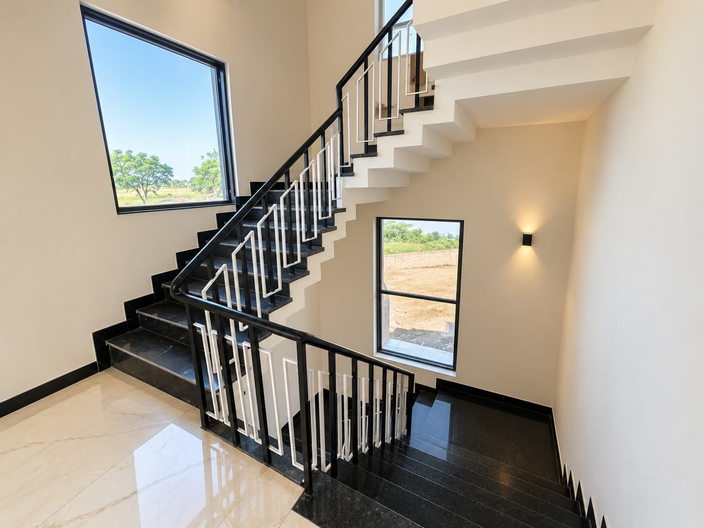 A modern staircase with black railings and white steps, leading to a landing with a view of a field.