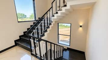 A modern staircase with black railings and white steps, leading to a landing with a view of a field.