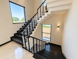 Una escalera moderna con barandillas negras y peldaños blancos, que conduce a un rellano con vistas a un campo.