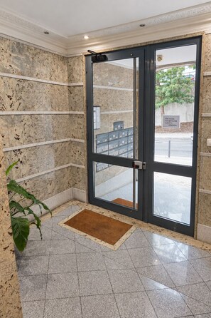 A hotel entrance with a marble wall, a glass door, and a doormat. - Cavaleiros Premiun Stay (Santo António dos Cavaleiros)