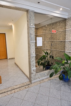 A lobby with a marble column, a glass elevator, and potted plants. - Cavaleiros Premiun Stay (Santo António dos Cavaleiros)