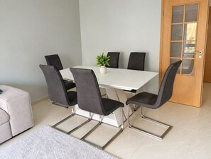 A dining area with a white table, black chairs, a small potted plant, and a wooden door with glass panels. - Cavaleiros Premiun Stay (Santo António dos Cavaleiros)