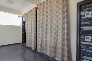 A corridor with patterned curtains, a tiled floor, and a door with a picture frame.