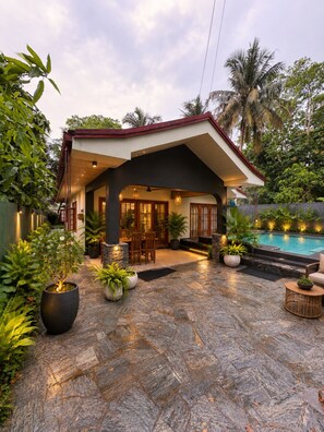 Ein modernes Haus mit Pool, Steinterrasse und tropischen Pflanzen.