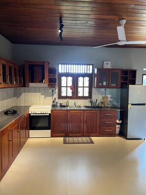 A kitchen with wooden cabinets, a stove, a refrigerator, and a window with decorative glass panes. - 3-bedroom house with AC in lovely Ahangama (Ahangama)