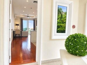 A hotel room with a wooden floor, a dining area with a table and chairs, a ceiling fan, and a window with a view of greenery. - Spacious 75 sqm apartment in quiet Karon, shared pool (Tambon Karon)
