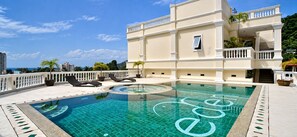 A rooftop swimming pool with lounge chairs and a building with balconies. - Spacious 75 sqm apartment in quiet Karon, shared pool (Tambon Karon)