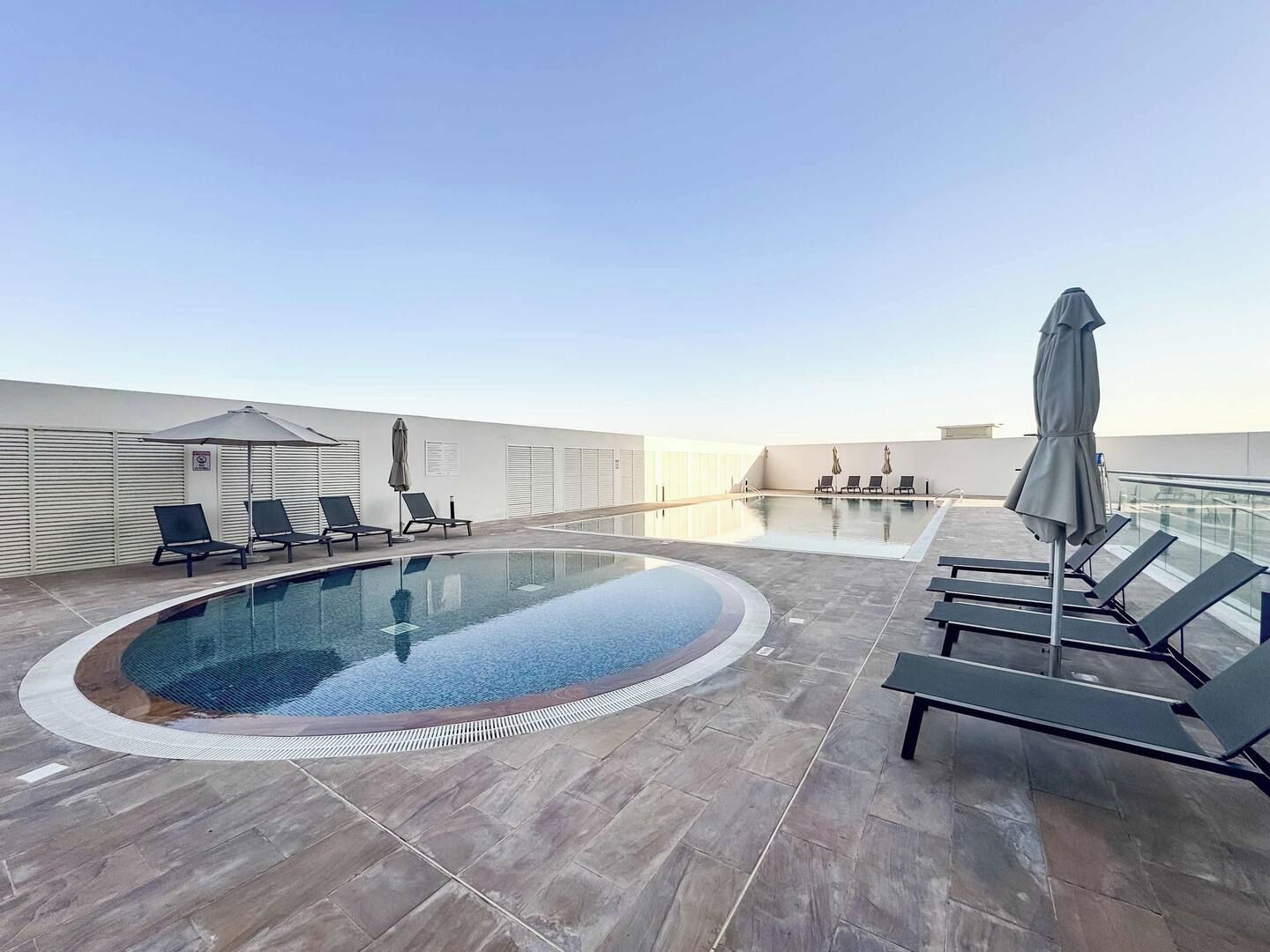 Une piscine à débordement située sur le toit, agrémentée de chaises longues et de parasols, le tout entouré par la façade d’un immeuble moderne.