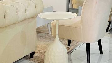 Un salon moderne avec un canapé, une table ronde, un fauteuil, un téléviseur et un vase rempli de fleurs.