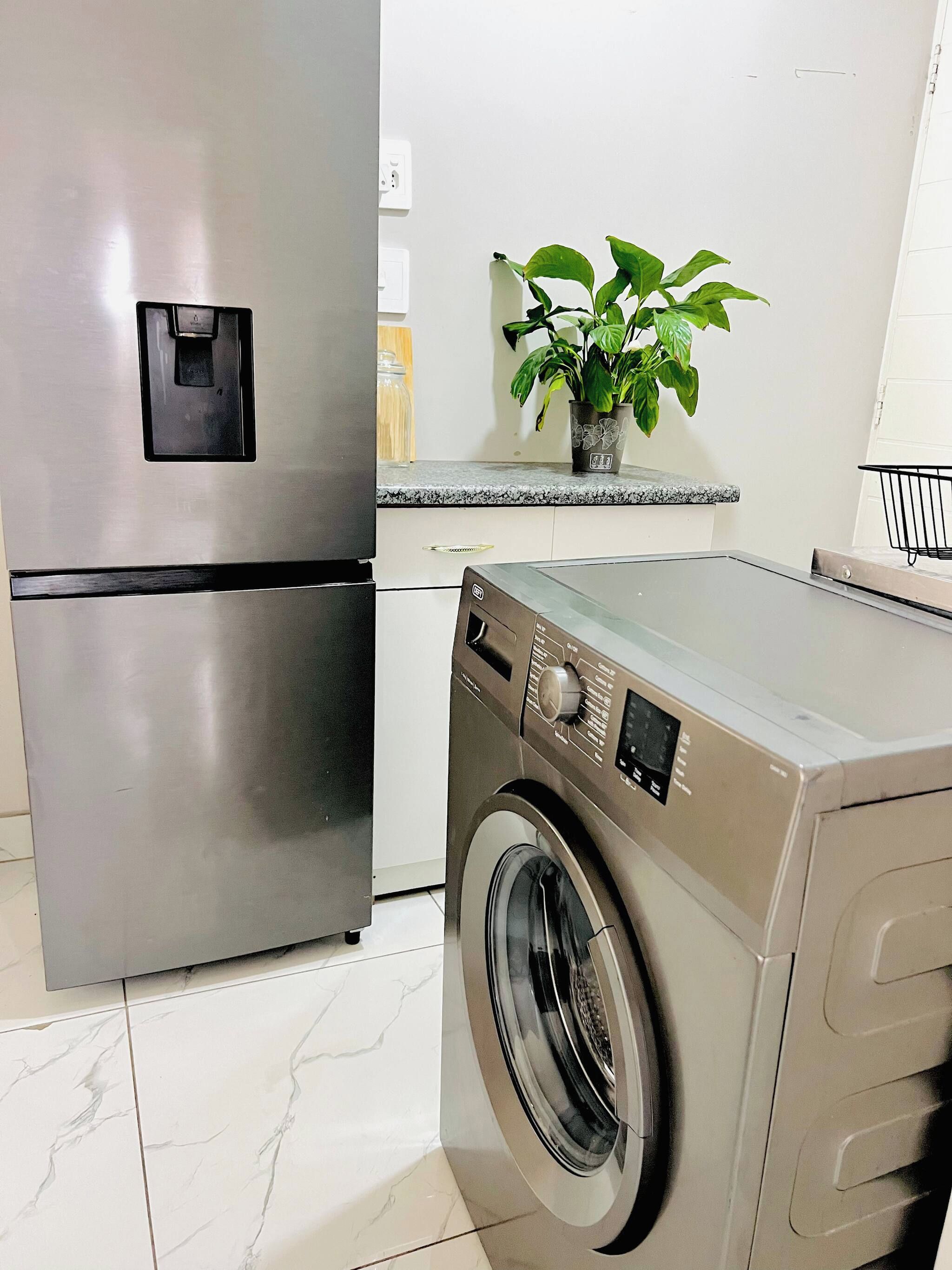 Una cocina con un refrigerador de acero inoxidable, una lavadora y una planta en maceta sobre la encimera.