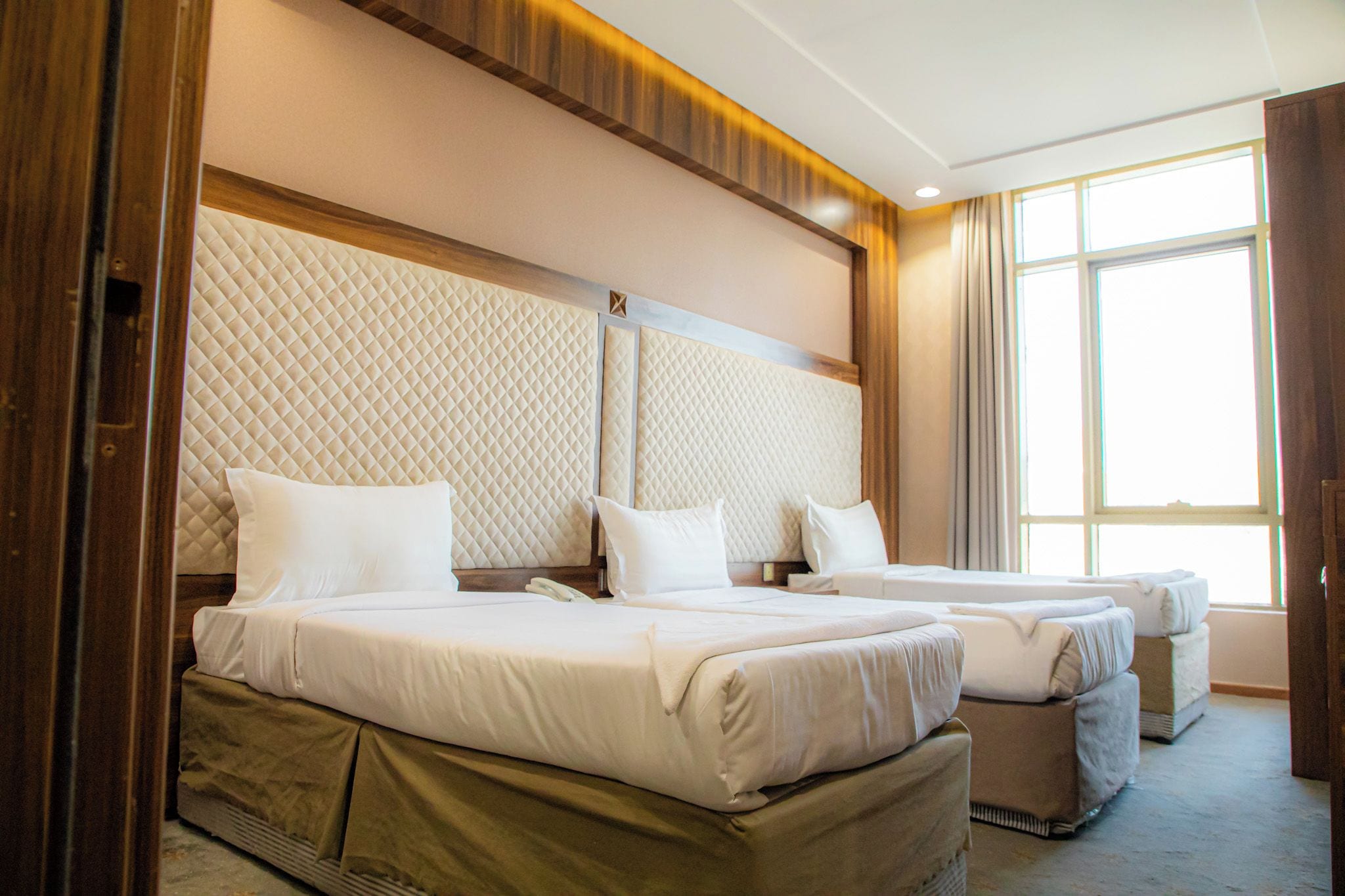 Ein Hotelzimmer mit einem großen Bett, einem kleineren Bett und einem Fenster mit Vorhängen.