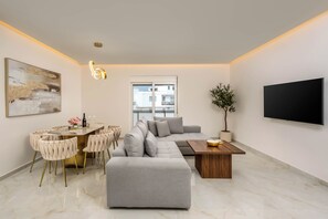 A modern living room with a grey sofa, a dining area with a marble table, and a large TV mounted on the wall. - Annamaria's Apartment (Rodos)