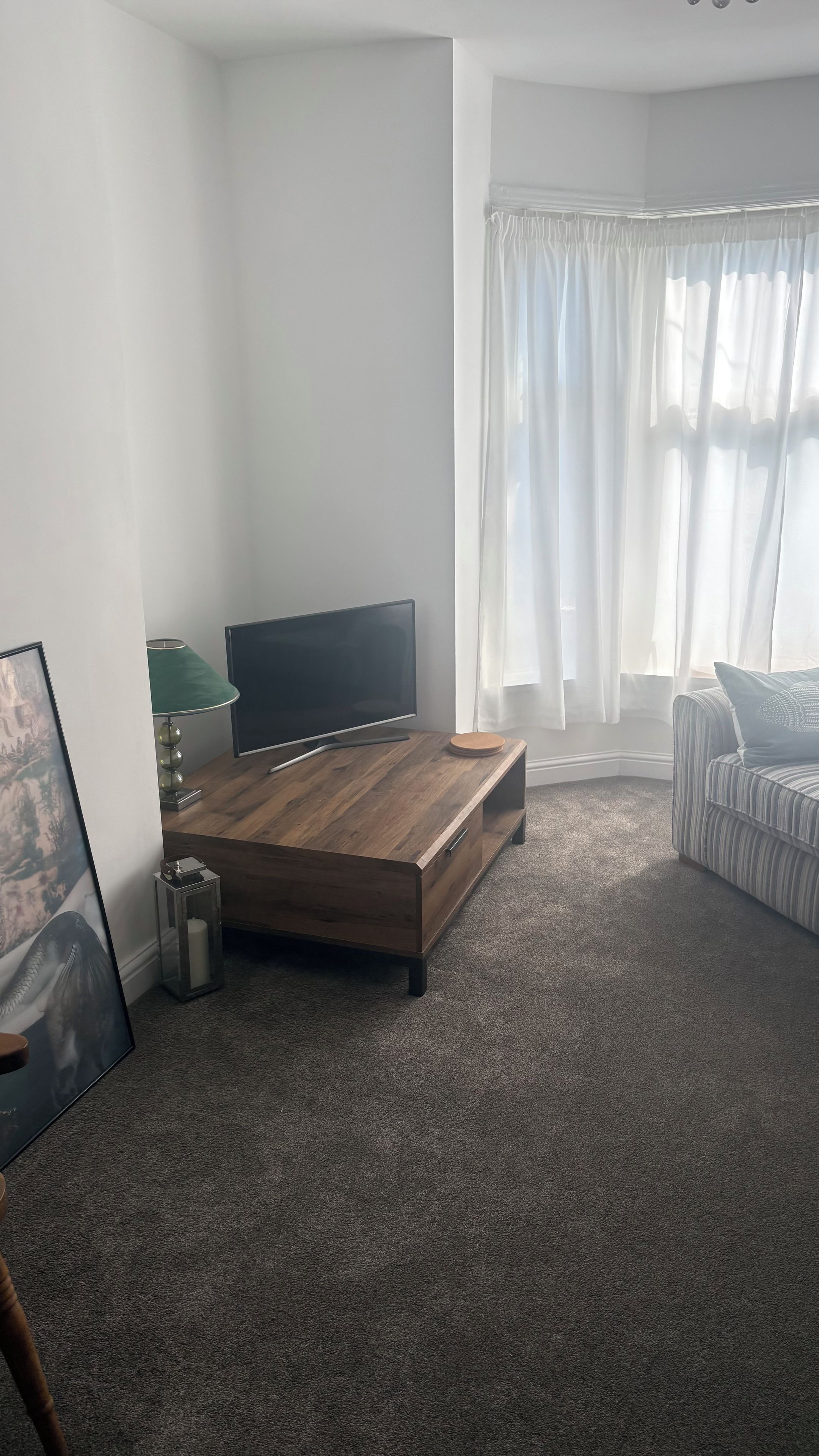A modern living room with a wooden coffee table, a flat-screen TV, a striped sofa, and a window with sheer curtains.