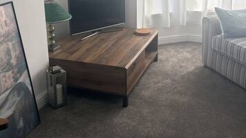 A modern living room with a wooden coffee table, a flat-screen TV, a striped sofa, and a window with sheer curtains.