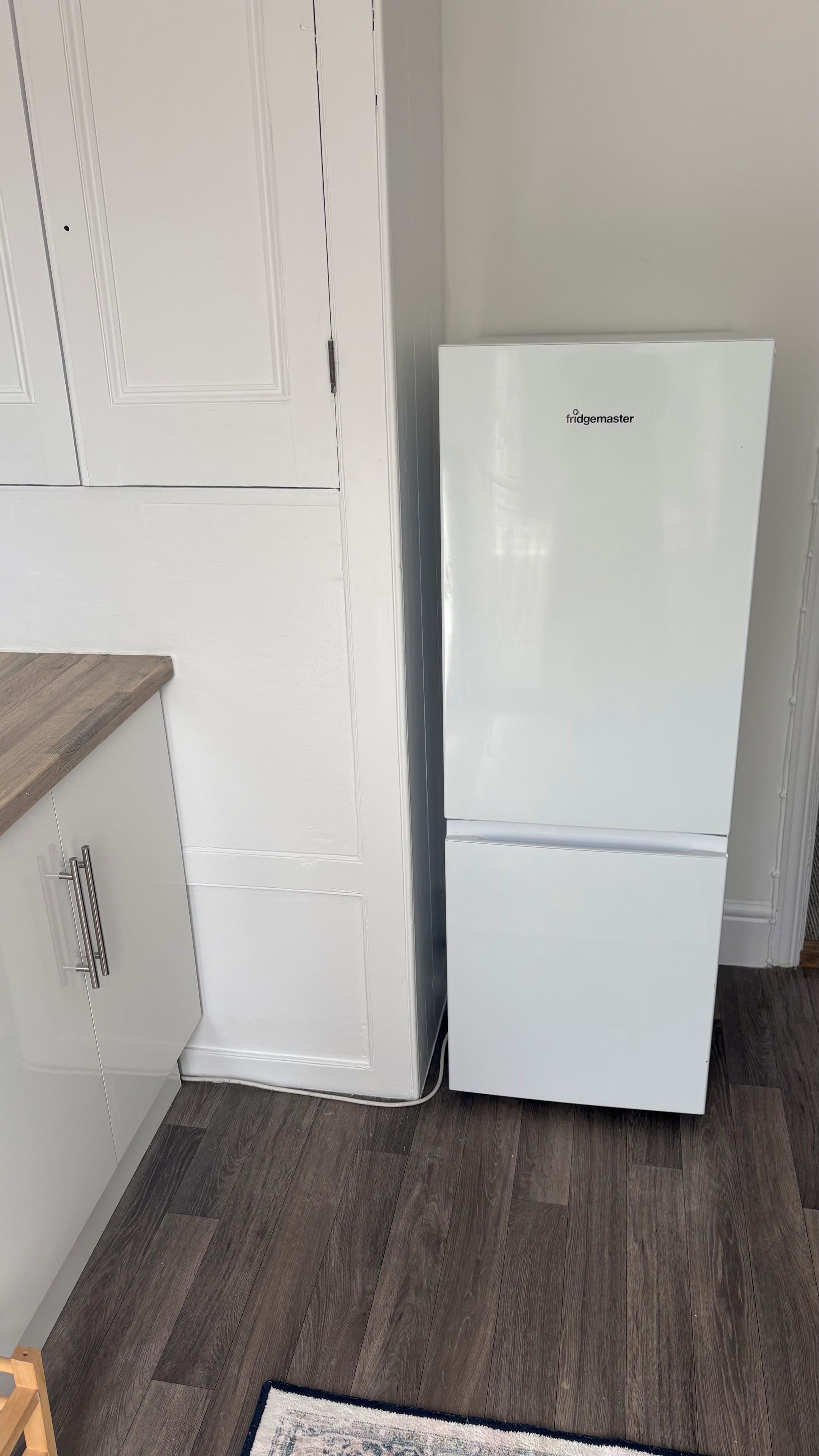 Ein weißer Kühlschrank mit Logo, eine Holzauskładung und ein dunkler Holzboden.