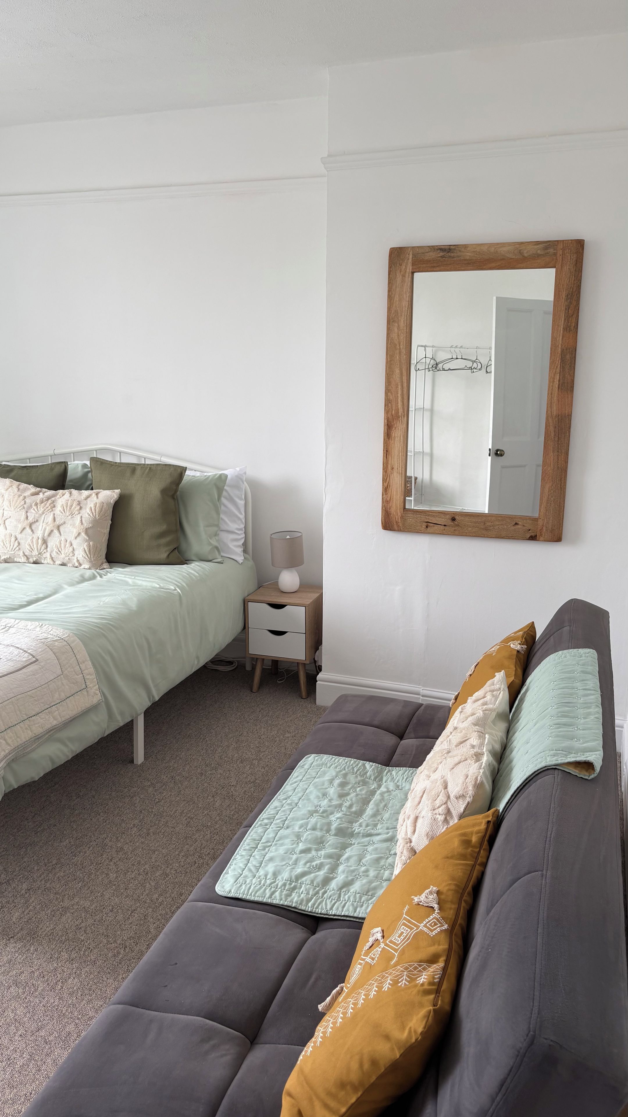 A bedroom with a bed, bedside table, lamp, and a large mirror on the wall.