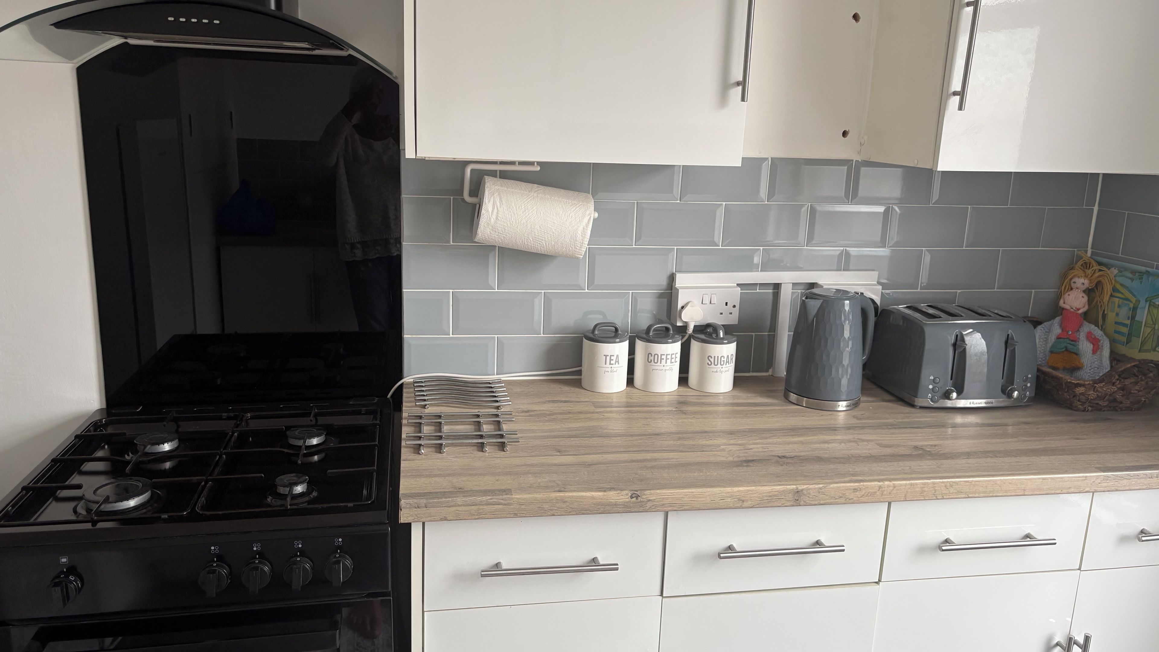 A kitchen with a gas stove, white cabinets, grey tiled backsplash, and a toaster.